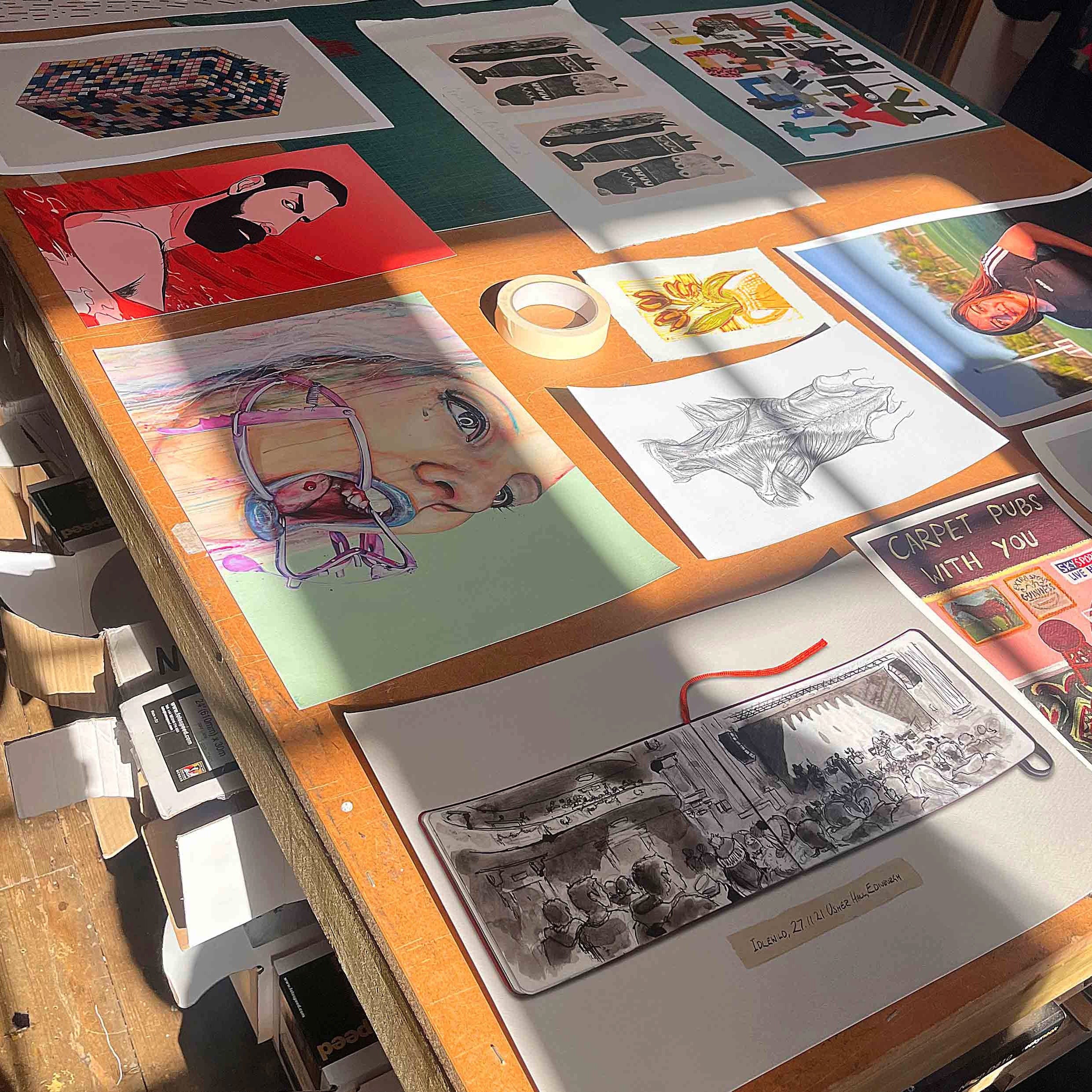 Tabletop with various artworks and drawings on a wooden surface