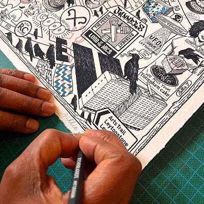 Person holding a pen over a collage of black and white illustrations on a green cutting mat.